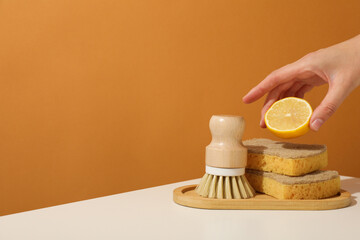 Sponges, brush and lemon in hand on brown background, space for text