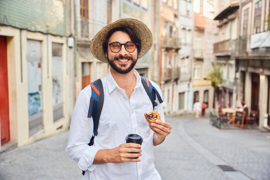 Smiling young man holding coffee cup and traditional dessert pastel de nata