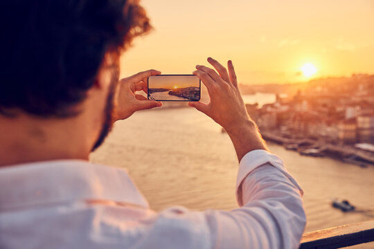 Man photographing Porto city through smart phone at sunset in Portugal