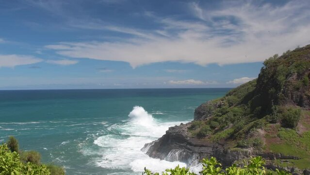 Large waves created by an offshore storm crash onto the cliffs on Kauai near Kilauea. Tropic birds roam the cliff side.