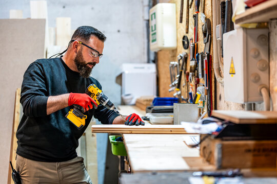 Carpenter using drill machine on wooden plank at workshop