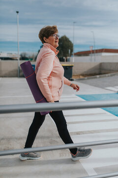 Active senior woman with exercise mat walking on footpath