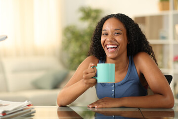 Happy black woman drinking and laughing at home