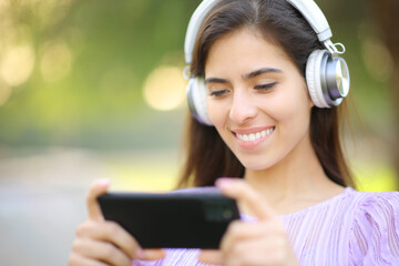 Happy woman watching video on phone wearing headphone - 761245798