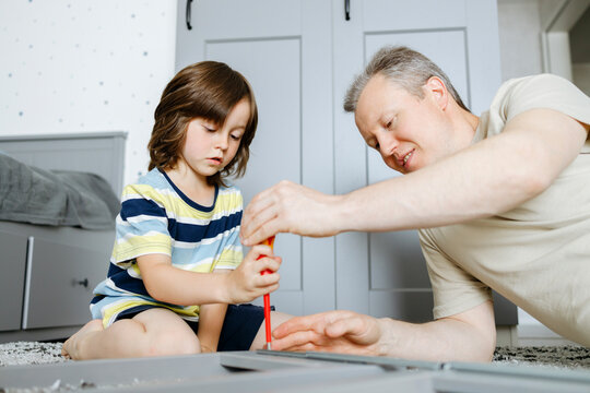 Son assembling nightstand using screwdriver with father at home