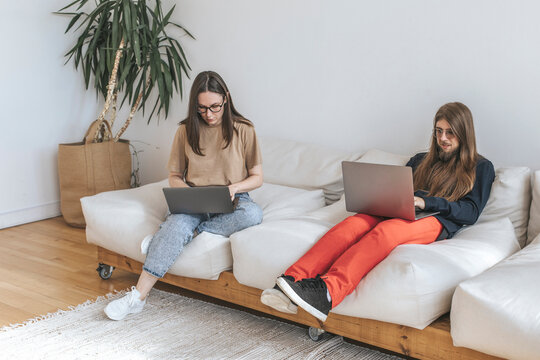 Programmers sitting on sofa coding through laptops at creative office