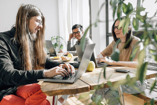 Team of IT technicians sitting at table coding on laptops in office