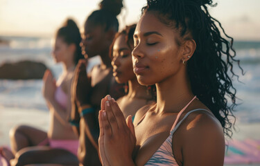 Group of young women doing yoga on the beach at sunrise, their eyes closed and hands in a prayer pose