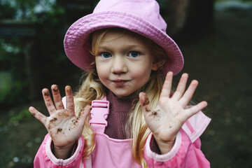 Girl in pink raincoat and hat showing dirty hands