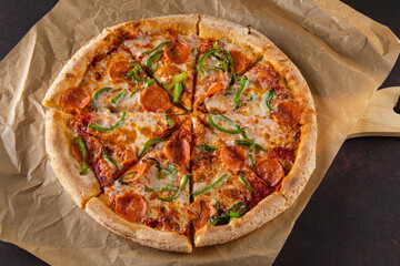 beautiful colorful pepperoni pizza on thin dough with sausages and sweet peppers lies on parchment on a board on a black background