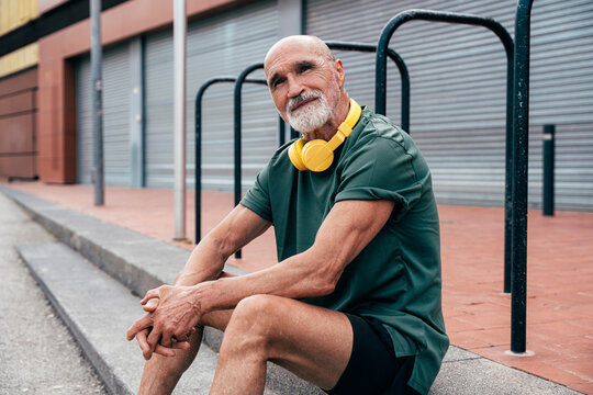 Senior man with wireless headphones sitting on steps
