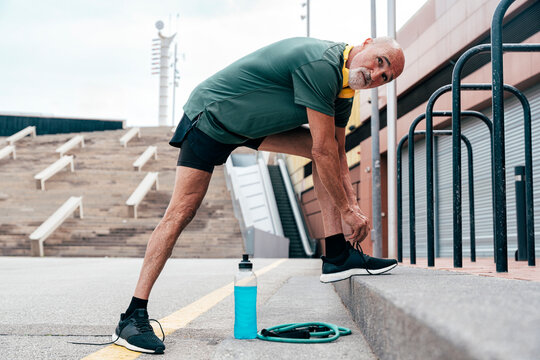 Retired senior man tying shoelace by parallel bars