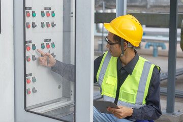 Electrical engineer man using tablet checks switchboard main Distribution Boards control panel electric factory building. Male Industrial technician worker working power distribution room.