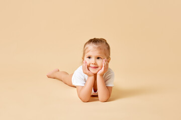 Portrait of charming pretty child, cute little girl put her head on hands against pastel color background. Baby with curious expression. Concept of childhood, motherhood, life, birth. Copy space. Ad