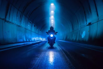 Tuinposter A motorcyclist in a blue-lit tunnel at night. © Oleksandr