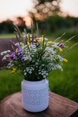 White outdoor vase with meadow flowers, herbs and grass. A colorful variety of summer wildflowers.