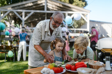 Grandfather teaching kids to cut vegetables for grilling. Grilling together at garden BBQ....