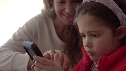 Mother teaching autistic daughter to use cellphone at home. - Powered by Adobe