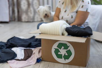 A woman with a dog sorts her clothes while sitting on the floor at home. A woman puts clothes she...