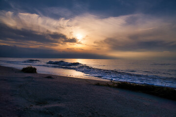 Sunset, illuminated sea. Sandy beach in the foreground. Light waves. Baltic Sea
