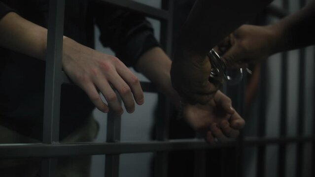 Warden takes off handcuffs from young prisoner. Multi ethnic teenagers serve imprisonment term in correctional facility or detention center. Young inmates in prison cell. Justice system. Close up.
