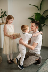 Fototapeta premium Son hugging and greeting father. Daughter gives present box gift smiling dad. Child makes surprise for Fathers Day. Children congratulate daddy in kitchen. International Mens Day. Happy family holiday