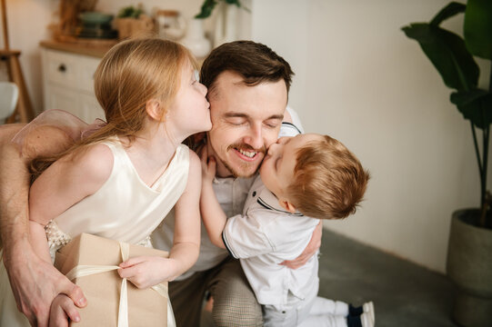 Child congratulate and kisses daddy closeup. Children kissing, hugging, greeting happy father. Daughter embraces smiling dad and give present box gift. Son makes surprise for Fathers Day. Happy family