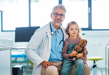 Portrait of a pediatrician with a little patient sitting on his knee. Friendly relationship between...