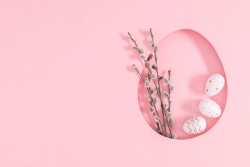 Easter composition. Frame is made in form of an egg and Easter decorations, sprig of fluffy willow and Easter egg on pastel pink background. Top view. Flat lay.