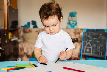 a small boy draws on sheets of paper lying on the table with colored pencils