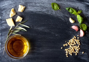 Ingredients for cooking italian pasta shot on dark stone background. Panorama of Italian cuisine with space for text. The composition includes olive oil, pine nuts, basil, flour, garlic, and parmesan 