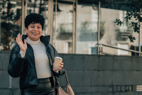 middle aged black woman drinking coffee and waving outside