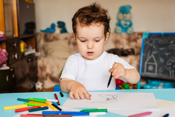 a small boy draws on sheets of paper lying on the table with colored pencils