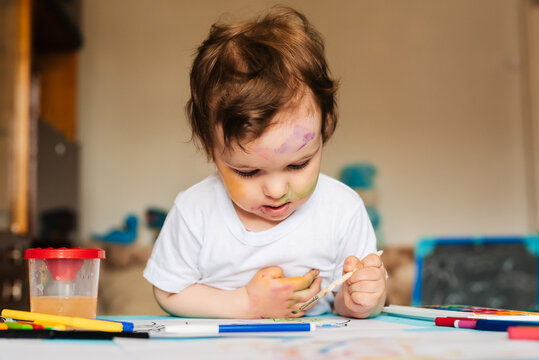 a small cute boy paints with brushes and colored paints on a sheet of paper