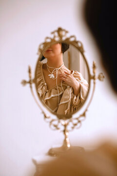 Young female looking at herself in the vintage mirrow and touching her necklace. Copy space for text. Beauty and fashion