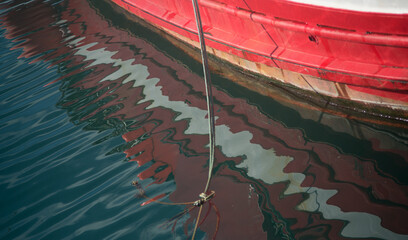 The red and white side of the boat is reflected in the sea water - 761295923