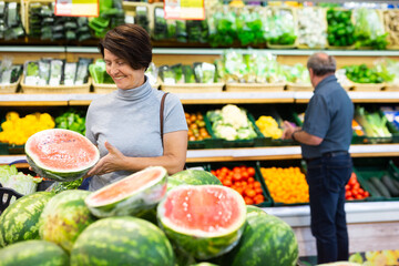 Elderly woman chooses watermelon in fruit and vegetable section