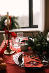 Beautiful New Year decor, a Christmas table with a red tablecloth and candles, festive dishes and glasses