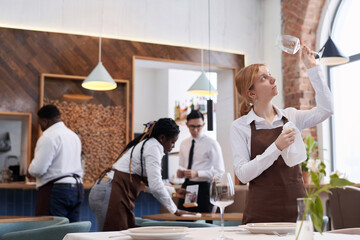 Selective focus shot of ethnically diverse waiting staff cleaning tables and polishing glassware in...