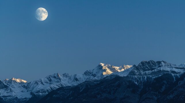 The moon above snowcapped mountains.