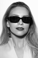 Fashion, make-up and lifestyle concept. Beautiful woman close-up studio portrait with sunglasses looking at camera. Model wearing white suit in bright studio background. Black and white image