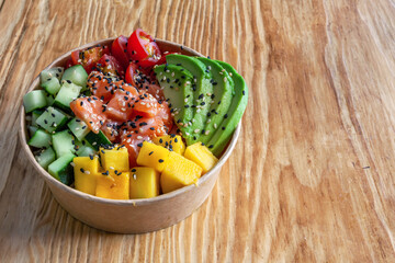 Takeaway poke bowl with fresh salmon, avocado, mango and vegetables in recycled kraft paper...