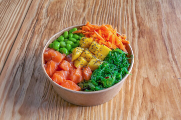Salmon poke bowl with wakame , rice, edamame beans on wooden background