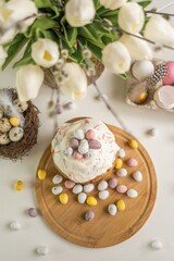 Easter cake decorated with colored pastel quail eggs on a wooden tray. Spring flowers tulips and willow branches in a beautiful vase. Easter decor, composition, painted eggs. Soft focus, top view