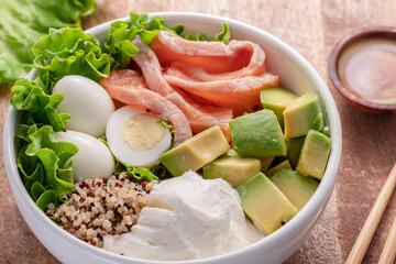 Salmon quinoa bowl with greens and vegetable on the wooden table. Balance in bowl.  Top view.