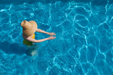 Woman in a big hat and yellow swimsuit chilling in swimming pool