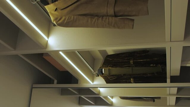 Dressing room with shelves. Summer dresses hanging on shelves, led lighting illuminate the wardrobe. Vertical video
