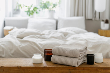Selective focus on wooden shelf with towels and candles against blurred bedroom interior