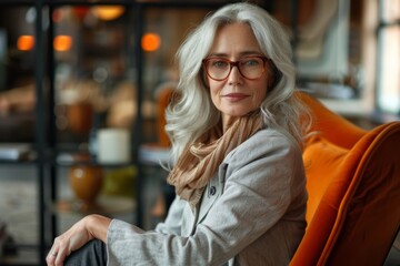 A respectable gray-haired office woman in a chair in an expensive, bright office.