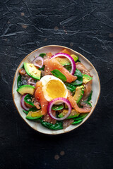 Salmon, avocado and egg salad with fresh leaves and onions, overhead flat lay shot on a black slate background - 761333589